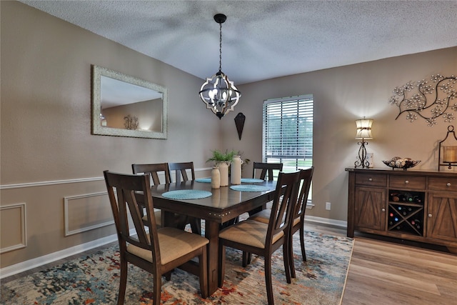 dining area featuring a chandelier, a textured ceiling, light wood-style flooring, and baseboards