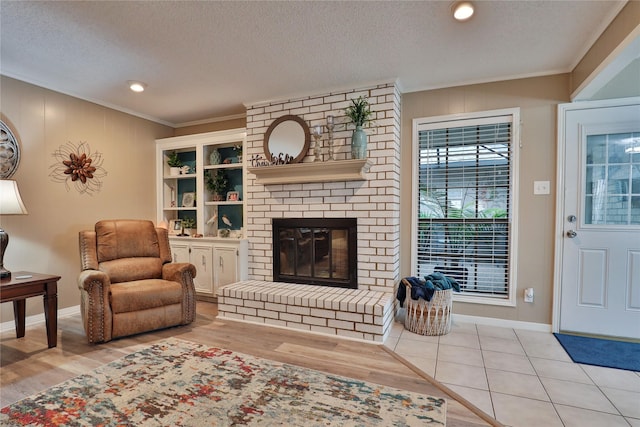 living room featuring crown molding, light wood-style floors, baseboards, a fireplace, and a textured ceiling