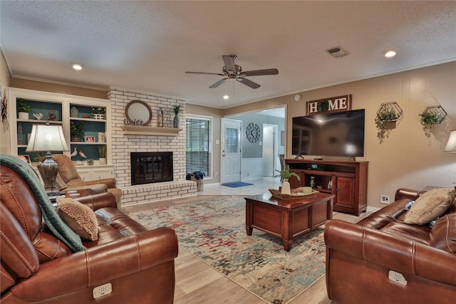 living area with a ceiling fan, ornamental molding, a textured ceiling, wood finished floors, and a brick fireplace