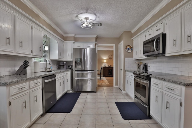 kitchen with appliances with stainless steel finishes, a sink, white cabinetry, a textured ceiling, and backsplash