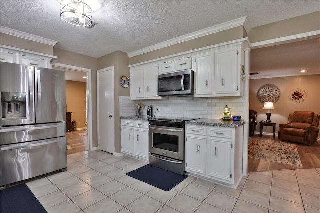 kitchen with stainless steel appliances, light tile patterned flooring, white cabinets, decorative backsplash, and a textured ceiling