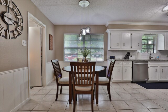 dining space with a textured ceiling, a wainscoted wall, crown molding, a chandelier, and light tile patterned floors