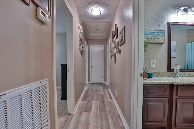 hallway with attic access, light wood-style floors, baseboards, and a textured ceiling