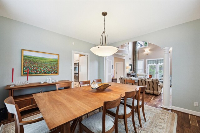 dining room with ornate columns, arched walkways, wood finished floors, and baseboards