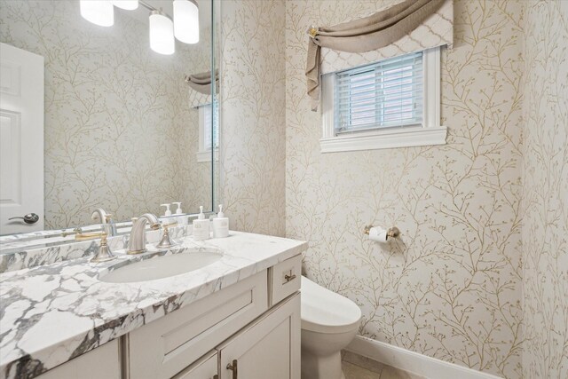 bathroom featuring toilet, vanity, wallpapered walls, tile patterned flooring, and baseboards