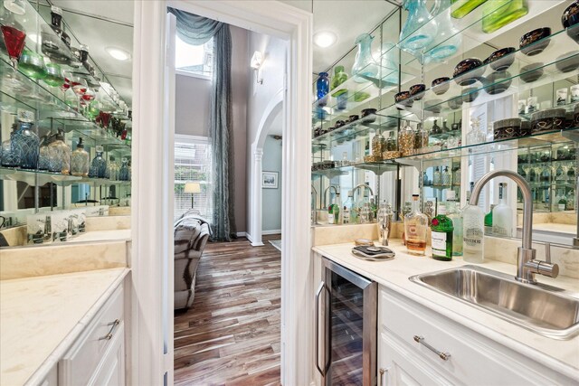 indoor wet bar featuring wine cooler, wood finished floors, plenty of natural light, and arched walkways