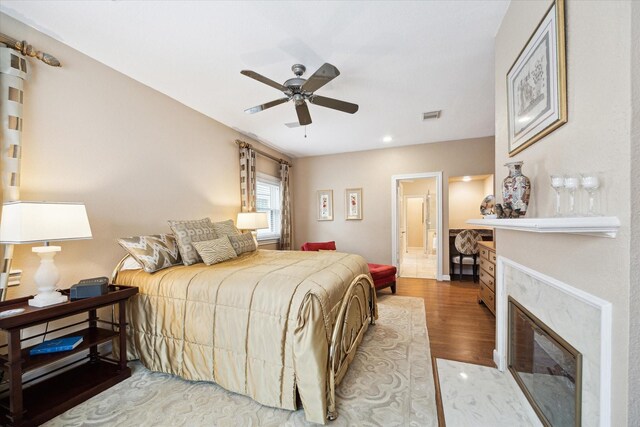 bedroom featuring wood finished floors, a fireplace with flush hearth, connected bathroom, ceiling fan, and recessed lighting
