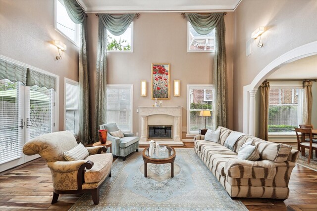 living room with arched walkways, a towering ceiling, a high end fireplace, wood finished floors, and decorative columns