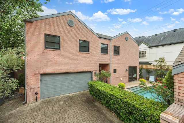 back of property featuring brick siding, a garage, and decorative driveway