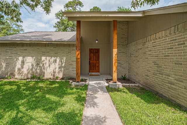 entrance to property with brick siding, a yard, and roof with shingles