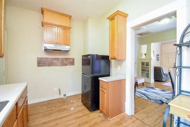 kitchen with freestanding refrigerator, under cabinet range hood, light wood finished floors, light countertops, and ornate columns