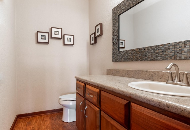 half bath featuring vanity, wood finished floors, toilet, and baseboards