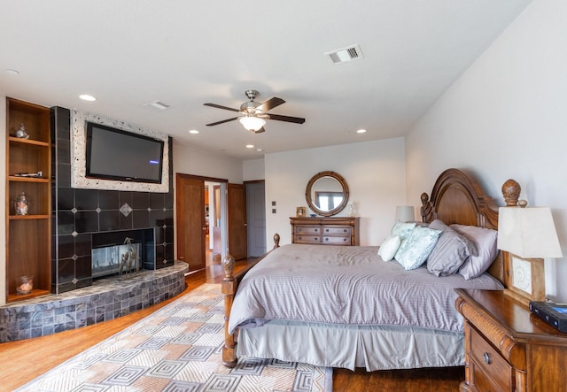 bedroom with wood finished floors, a large fireplace, recessed lighting, and ceiling fan