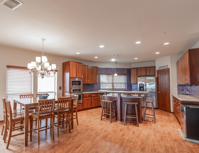 kitchen featuring stainless steel appliances, brown cabinetry, a chandelier, backsplash, and light wood finished floors