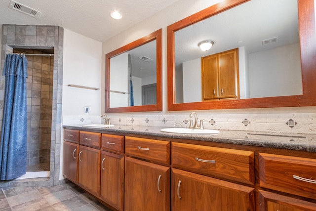 bathroom featuring a tile shower, double vanity, decorative backsplash, and a textured ceiling