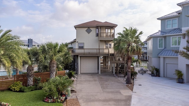 beach home featuring a balcony, concrete driveway, a standing seam roof, fence, and metal roof