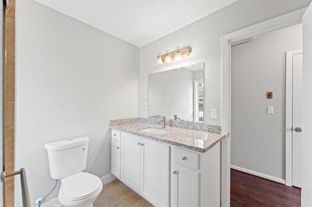 bathroom with toilet, vanity, baseboards, and wood finished floors