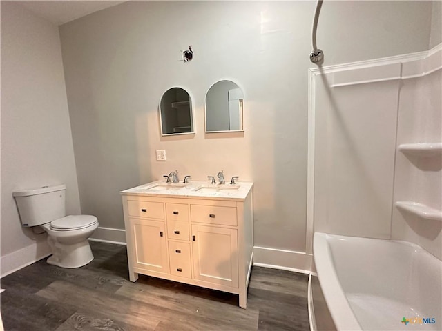 bathroom featuring wood finished floors, toilet, double vanity, baseboards, and tub / shower combination