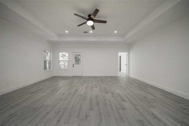 unfurnished living room featuring a tray ceiling, a ceiling fan, wood finished floors, baseboards, and recessed lighting