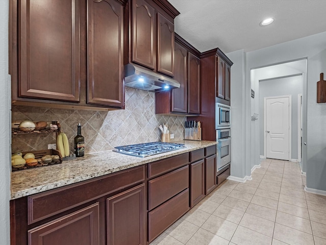 kitchen with appliances with stainless steel finishes, under cabinet range hood, baseboards, backsplash, and light tile patterned floors