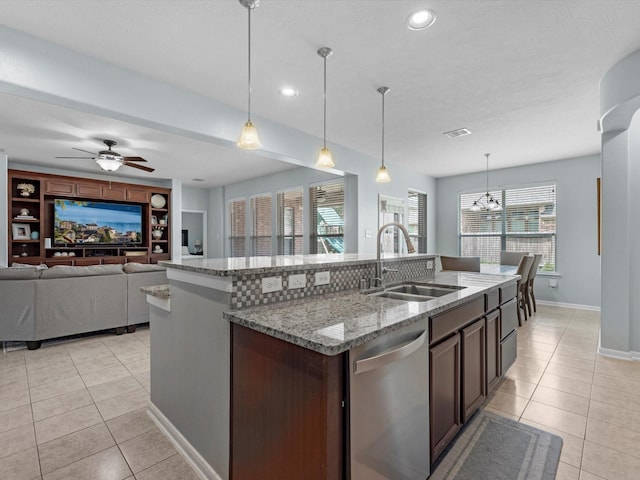 kitchen with stainless steel dishwasher, a sink, light tile patterned floors, an island with sink, and baseboards