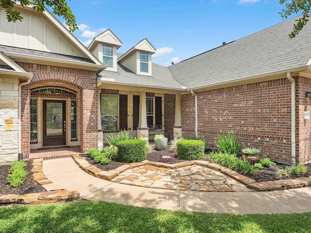 doorway to property featuring roof with shingles, brick siding, and stone siding