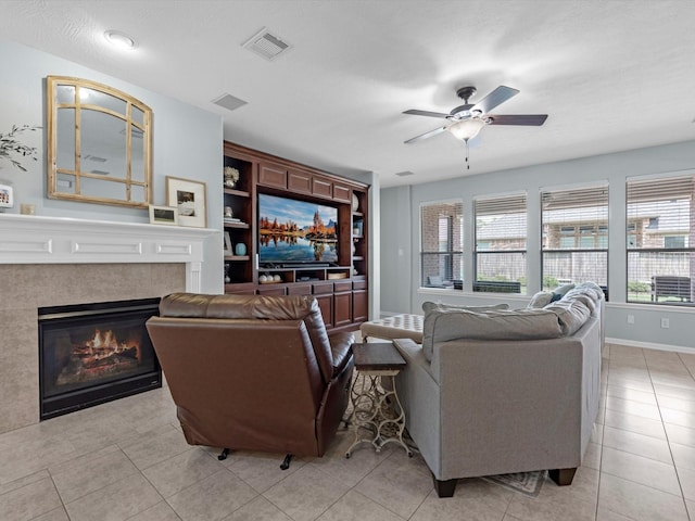 living area featuring a ceiling fan, a glass covered fireplace, light tile patterned flooring, and baseboards