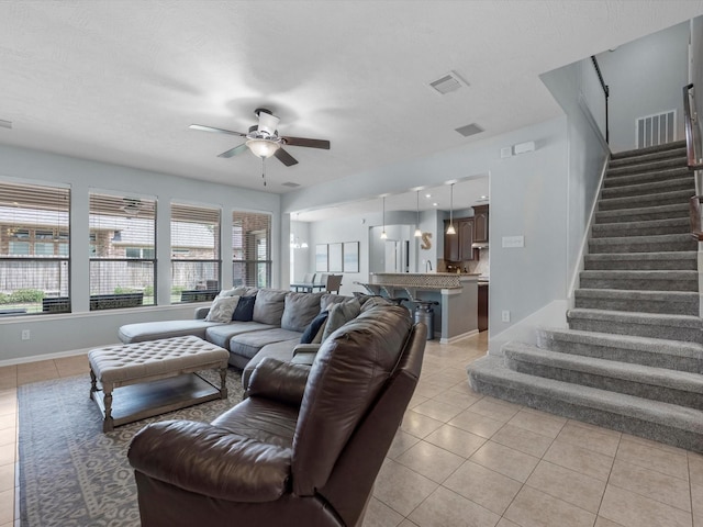 living area with light tile patterned floors, a ceiling fan, stairs, and baseboards