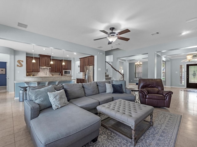 living area with light tile patterned floors, a chandelier, a ceiling fan, stairway, and baseboards