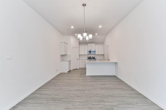 kitchen with stainless steel microwave, a chandelier, light countertops, tasteful backsplash, and white cabinets