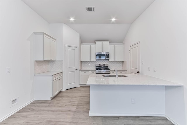 kitchen featuring appliances with stainless steel finishes, a sink, vaulted ceiling, a peninsula, and light stone counters