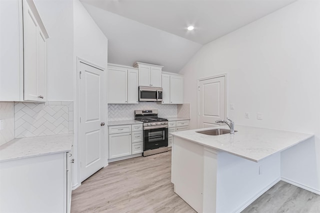 kitchen with appliances with stainless steel finishes, a sink, vaulted ceiling, a peninsula, and white cabinetry