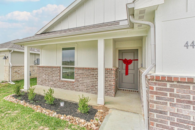 entrance to property featuring board and batten siding, covered porch, and brick siding