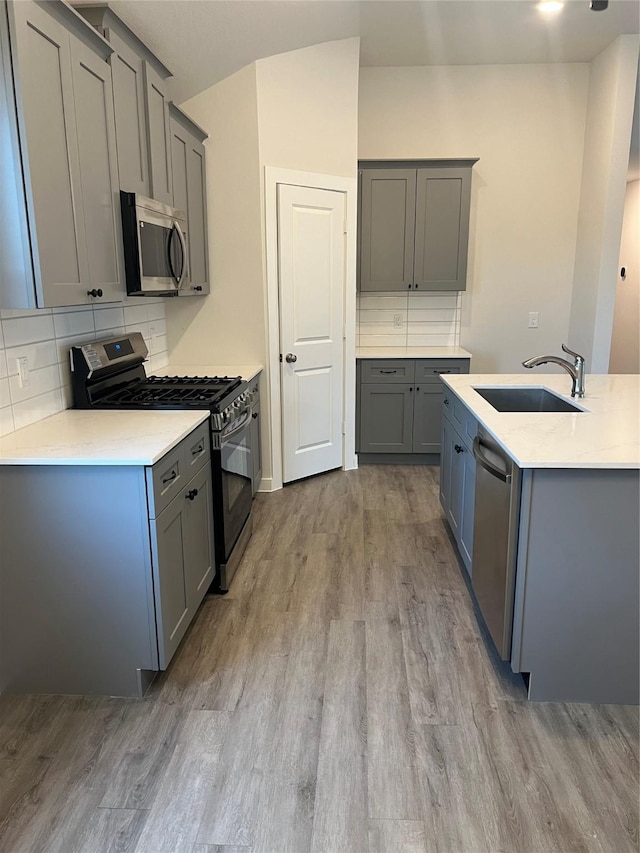 kitchen with stainless steel appliances, a sink, gray cabinets, and vaulted ceiling