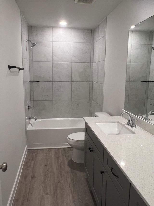 bathroom featuring wood finished floors, toilet, vanity, tub / shower combination, and baseboards