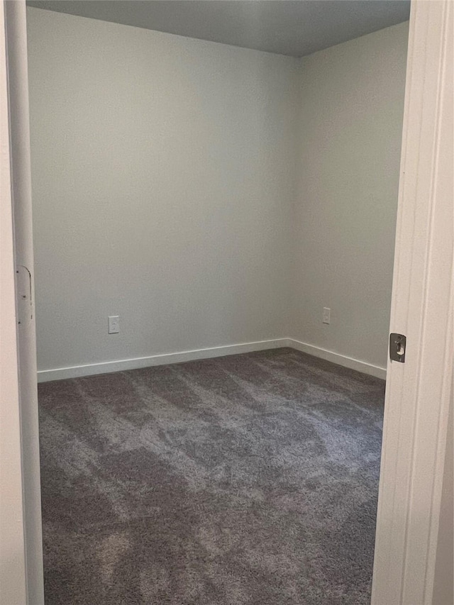 unfurnished room with dark carpet and baseboards