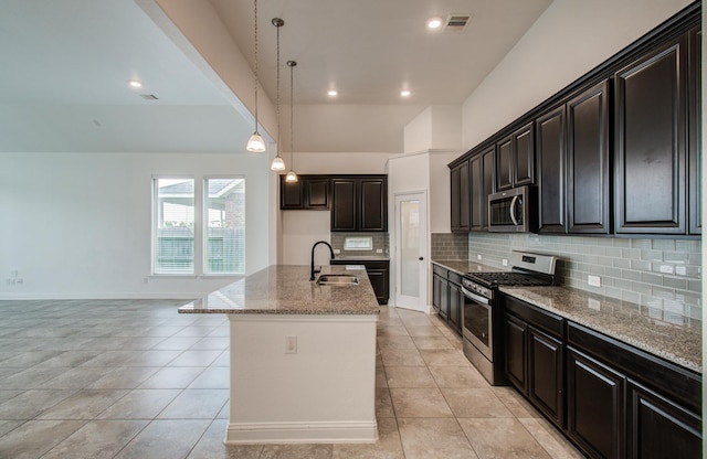 kitchen with stainless steel appliances, tasteful backsplash, light stone counters, a center island with sink, and light tile patterned floors