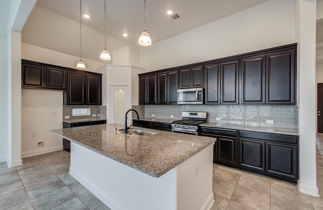 kitchen featuring appliances with stainless steel finishes, a sink, stone countertops, a center island with sink, and backsplash