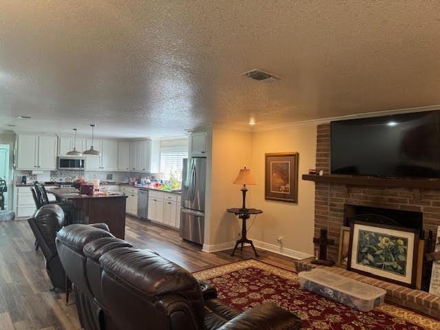 living area featuring a textured ceiling, dark wood-style flooring, a fireplace, crown molding, and baseboards
