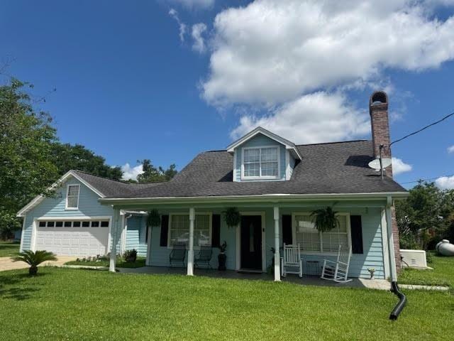 view of front of home featuring covered porch, a chimney, a front lawn, a garage, and driveway