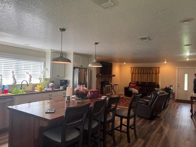 kitchen featuring stainless steel appliances, a textured ceiling, a sink, dark wood finished floors, and a kitchen island