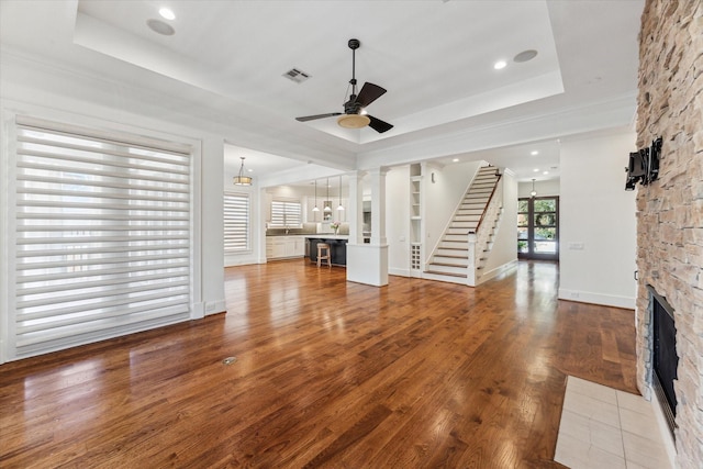 6216 Queenswood Ln, Houston, TX 77008 - unfurnished living room with a ceiling fan, wood finished floors, a stone fireplace, a tray ceiling, and stairs