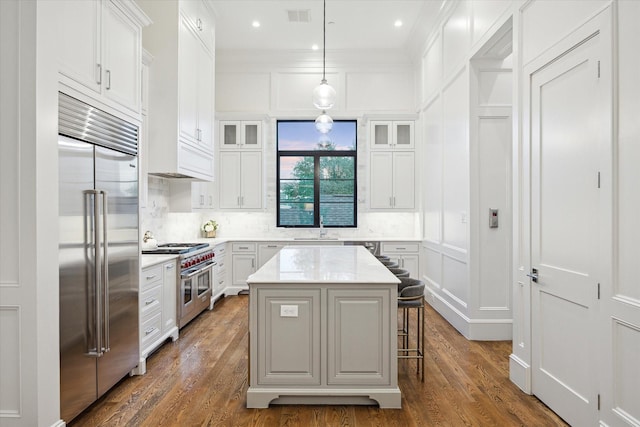 kitchen with premium appliances, a decorative wall, white cabinets, glass insert cabinets, and a sink