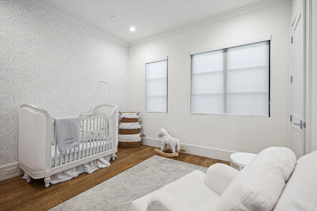bedroom with wallpapered walls, wood finished floors, a crib, baseboards, and ornamental molding