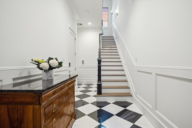 stairway featuring tile patterned floors, a decorative wall, ornamental molding, and wainscoting