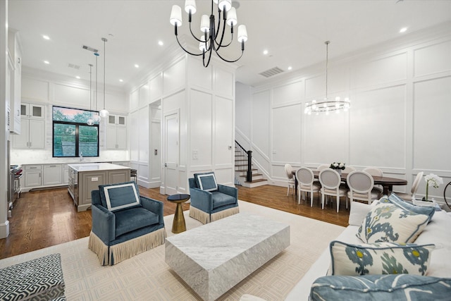 living area with a decorative wall, a chandelier, crown molding, wood finished floors, and stairway