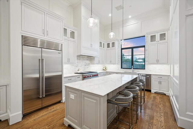 kitchen with high end appliances, a center island, a sink, white cabinetry, and ornamental molding