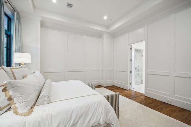 bedroom with a decorative wall, dark wood-type flooring, ensuite bathroom, and recessed lighting
