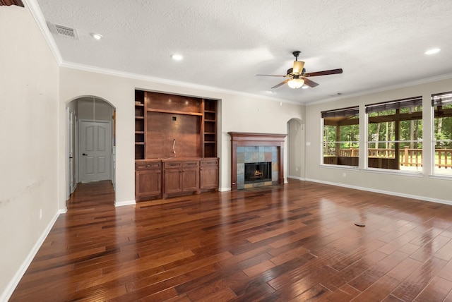 10 Hollow Glen Ln, Tomball, TX 77375 - unfurnished living room with arched walkways, a ceiling fan, a textured ceiling, a tiled fireplace, and dark wood finished floors