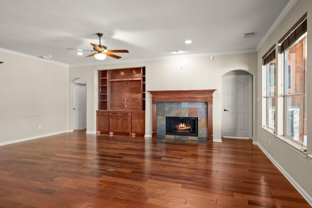 10 Hollow Glen Ln, Tomball, TX 77375 - unfurnished living room featuring arched walkways, a ceiling fan, a tiled fireplace, hardwood / wood-style flooring, and crown molding